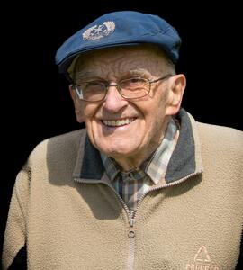 A photo of Gordon Wolfram grinning and wearing glasses, a blue cap, and a beige collared fleece.