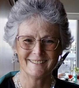 A headshot of Beverlee Sealey with short greying hair, glasses, and a necklace.