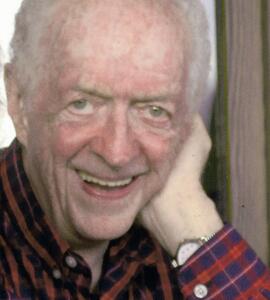 A headshot of Kenneth MacKenzie Campbell with short white hair and a red and blue collared shirt.