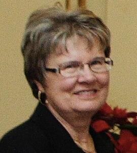 A headshot of Stephanie Brawn with short hair, glasses, and red flowers.