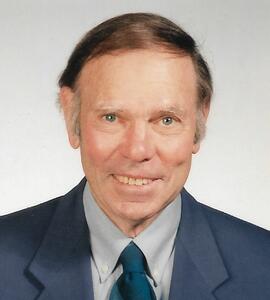 A headshot of John Skelton Belrose with short black hair and a blue suit and tie.