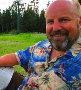 James Scott Beesley wearing a blue patterned shirt sitting on a grassy field