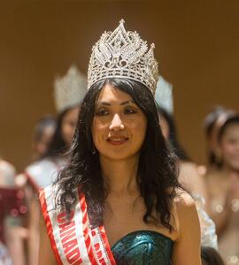 A photo of Wendy Leung wearing a green dress, red and white sash, and crown.