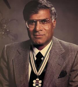 A portrait of Gurdev Singh Gill wearing a grey suit and a medal.