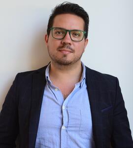 Photo of Fernando Rodríguez wearing a blue collared button-up, a black jacket, and glasses.