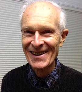 A headshot of Frederick William Wiley with white hair, wearing a black shirt and a plaid collared shirt.