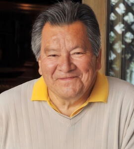 A portrait of Hemas Kla-Lee-Lee-Kla wearing a beige long sleeve shirt over a yellow collared shirt