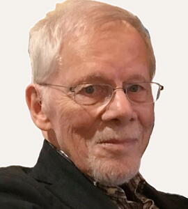 A portrait of David C. Whetter with short white hair, glasses, and a black collared jacket