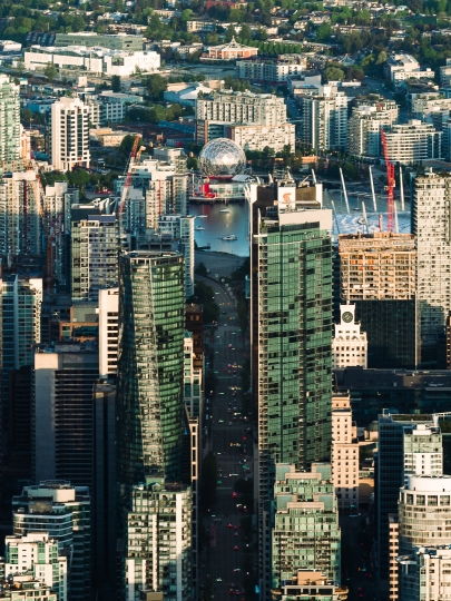 A photograph of Vancouver taken from a helicopter above the Stanley Park area. It shows West Georgia Street, with False Creek and Science World at the end, and East Vancouver in the background.