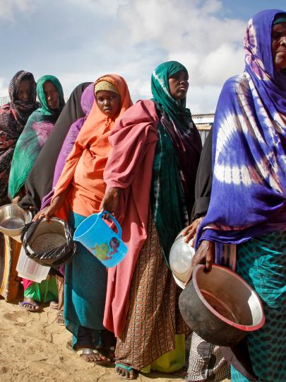 African women in shawls carrying empty containers queue up in desert 