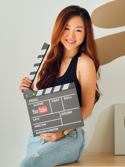 Asian woman leaning against desk and holding open a film clapboard