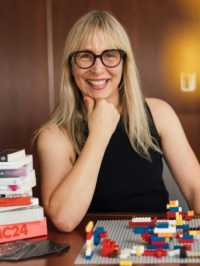 Dr. Kari Marken sits at a desk with lego, smiling at the camera.