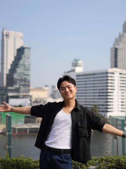 Sony Tsai posing with arms outstretched, with water and skyscrapers behind him