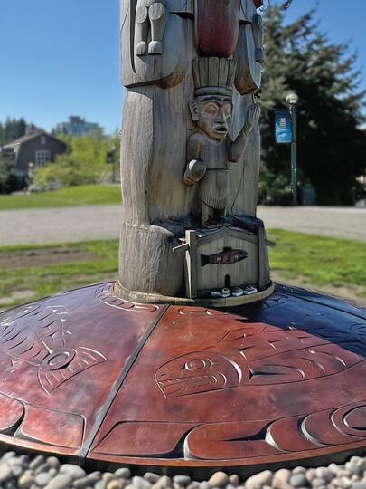 Indigenous bronze artwork at the base of a totem pole