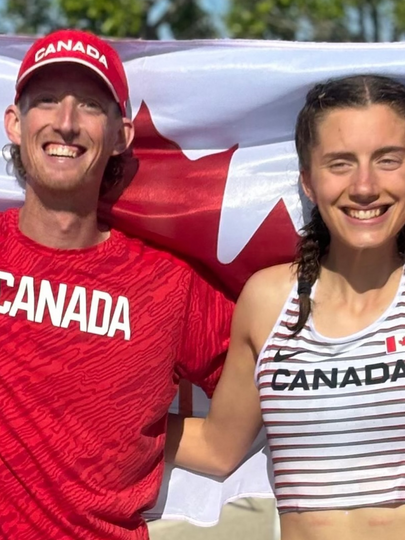 Evan Dunfee and Olivia Lundman, smiling and holding a large Canadian flag behind them