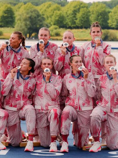 The Canadian women's rowing eight team pose on a dock while kissing their silver medals