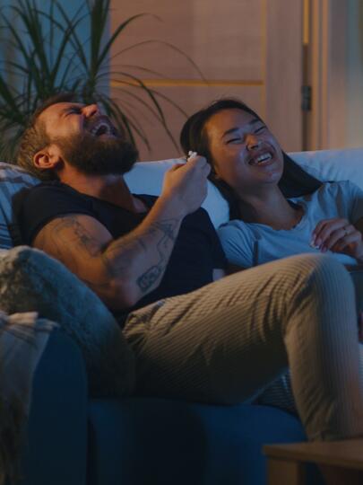 Man and woman laughing on couch in front of TV screen