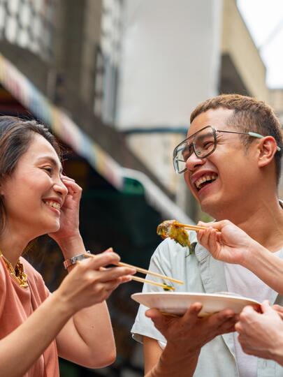 Two women and man eating from a plate with chopsticks