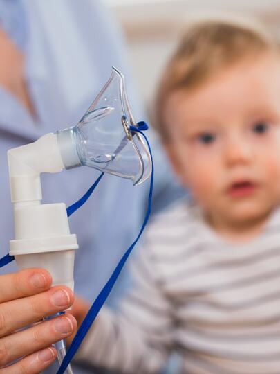 A baby sits in the lap of a nurse who is holding an oxygen mask