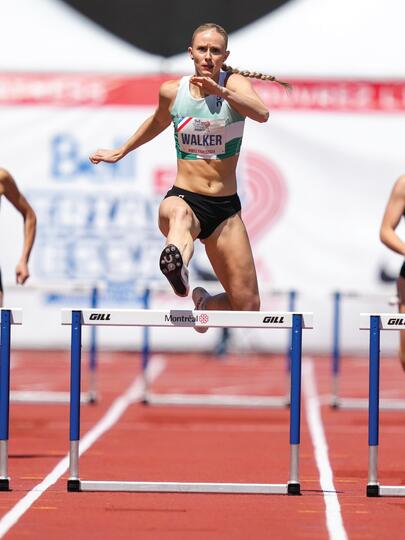 Five track-and-field athletes sprinting down a track with hurdles in each lane