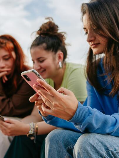 Young people sitting in a row outside looking at smartphones
