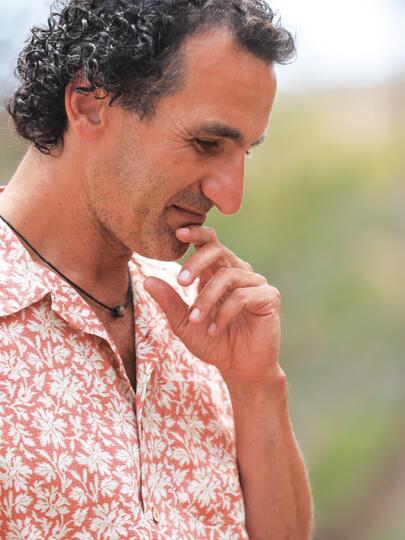 Simon Donner in a pink collared shirt, touching his chin with his finger, against a blurred grassy background.