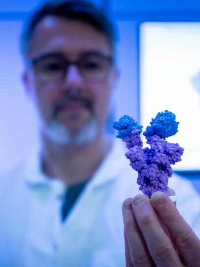 A person in a lab coat holding up a blue-violet crystalline structure