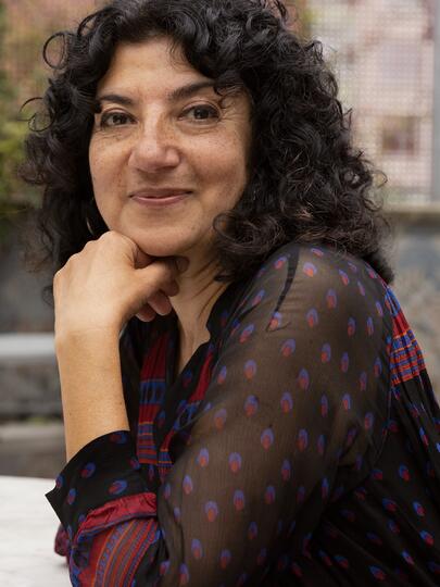 A portrait of Meeru Dhalwala with curly black hair and her chin propped in her hand.