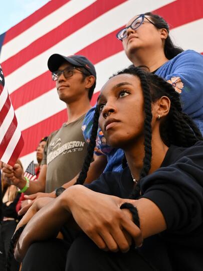 Supporters of Vice President Kamala Harris during her concession speech for the 2024 presidential election, with American flags in the background 