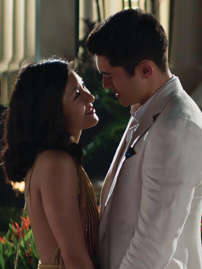 Asian woman and man in evening wear lean into a kiss