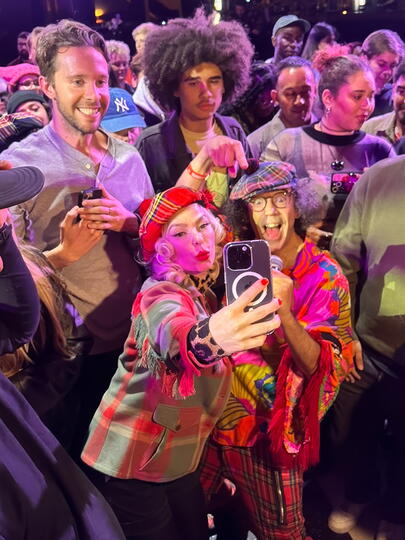 A fan poses with Nardwuar for a selfie, with people milling in the background