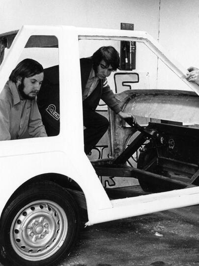 A black and white photo of three people working on the Wally Wagon