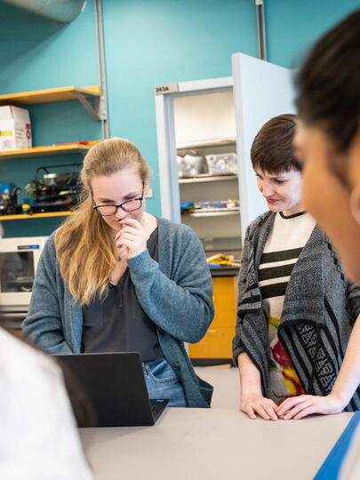 Three women gathered around fourth woman looking at laptop