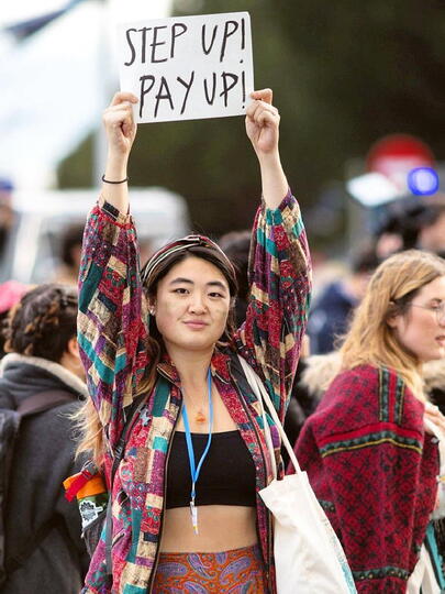 An image of Sophia Yang standing in front of a crowd with her arms up, wearing a lanyard, black top, and quilted red, green, and white top.