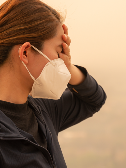 A person in a mask standing in hazy air holds a hand to their forehead