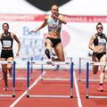 Five track-and-field athletes sprinting down a track with hurdles in each lane